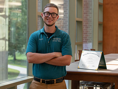 An alumnus standing in front of a table showing a diploma