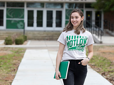 a woman wearing a Motlow t-shirt standing in front of a campus building