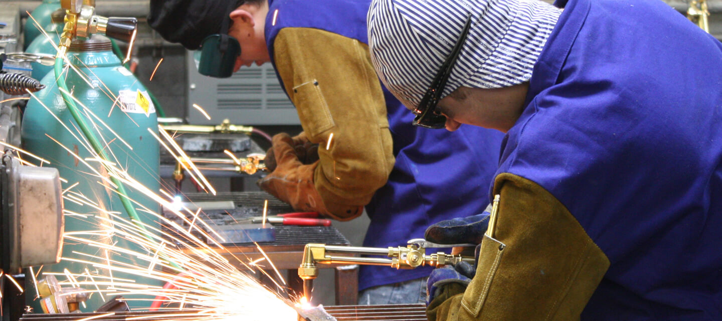 A man in a blue coat welds with sparks flying